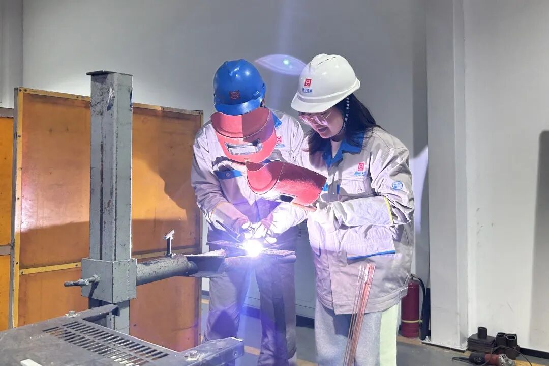 葛小青(左)指导记者手握焊枪进行焊接